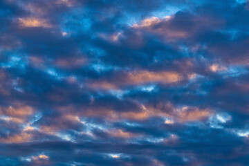 Naklejka na ściany i meble Dramatic clouds in blue sky, illuminated by rays of sun at colorful sunset to change weather. Soft focus, motion blur abstract meteorology background.