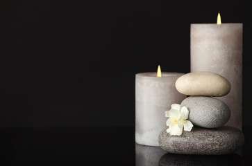 Stack of spa stones, burning candles and fresh flower on black background. Space for text