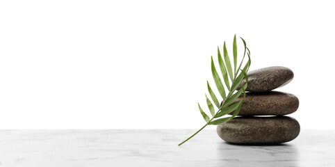 Stack of spa stones and tropical leaf on marble table against white background. Space for text