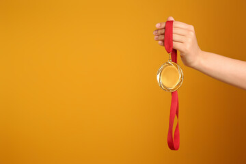 Woman holding gold medal on yellow background, closeup. Space for text