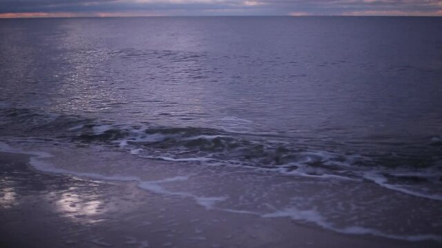 Cold winter windy Baltic sea coast beach in twilight purple light with dramatic cloudy sky and tranquil romantic waves. An HD video footage with audio