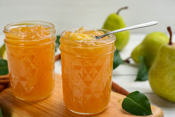 Delicious pear jam in glass jars on wooden board, closeup