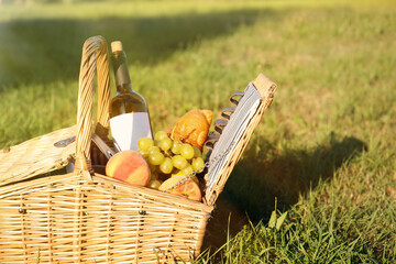 Picnic basket with snacks and bottle of wine on green grass in park