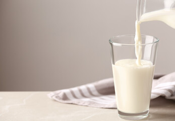 Pouring milk into glass on table against grey background. Space for text