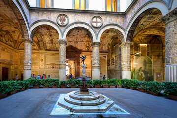 The first courtyard of the Palazzo Vecchio in Florence Italy with a small fountain with statue, frescoes on the wall and vaulted columns. - Powered by Adobe