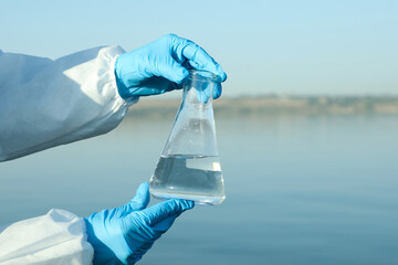 Scientist with conical flask taking sample from river for analysis, closeup