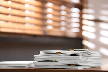 Stack of blank paper with binder clips on wooden table indoors. Space for text
