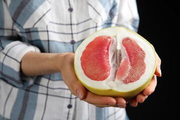 Woman holding half of fresh red pomelo on black background, closeup