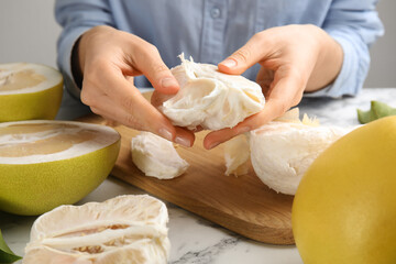 Woman with tasty ripe pomelo at white marble table, closeup