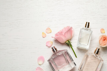 Flat lay composition with different perfume bottles and roses on white wooden background, space for...