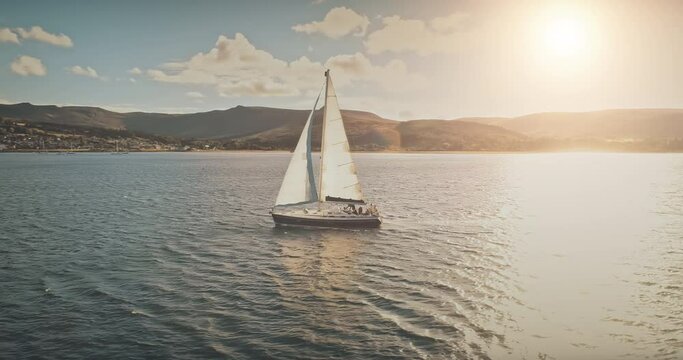 Luxury yacht race at sun light aerial. Yachting on serene seascape at open sea. Boat with big white spinnaker sail at ocean bay. Lonely ship cruise at water on summer sunny day. Cinematic drone shot