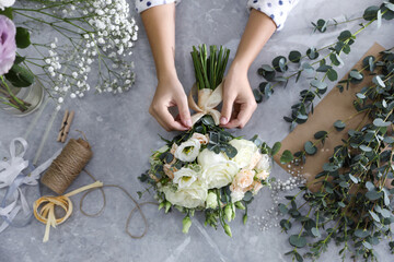 Obraz na płótnie Canvas Florist tieing bow on beautiful wedding bouquet at light grey marble table, top view