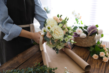 Florist making beautiful wedding bouquet at wooden table, closeup