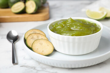 Feijoa jam and fresh fruit on white marble table, closeup