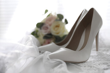 Fototapeta na wymiar Pair of white high heel shoes, veil and wedding bouquet on light background