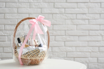 Wicker gift basket with cosmetic products on table near white brick wall. Space for text