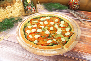 Side view of Italian pizza in Caprese salad style served on wooden plate with Christmas new year decoration on background. vegetarian dish with basil pesto sauce, tomato slices and mozzarella cheese
