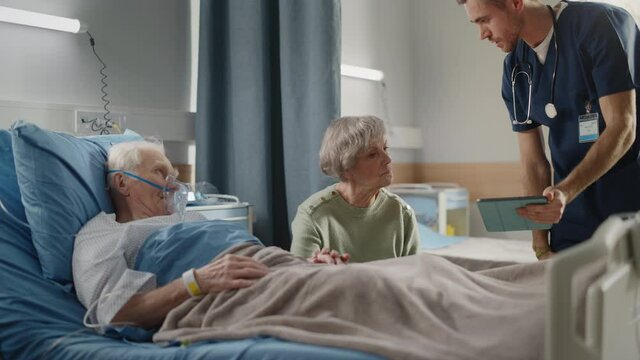 Hospital Ward: Elderly Patient Resting in Bed with Beautiful Caring Wife Supports Him, Doctor Uses Tablet Computer, Talks, Explains Test Results. Old Man Fully Recovering after Successful Surgery