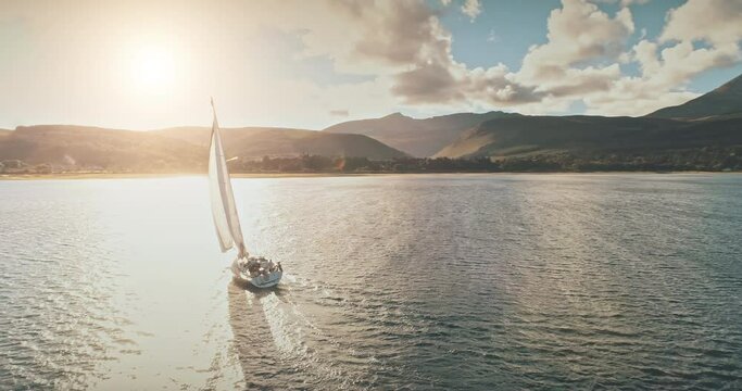 Sailing yacht in wind waves at Arran Island sea bay in Scotland. Amazing seascape at Brodick port city. Lonely sail boar race at sun shine with fluffy clouds. Serene water scape and transportation
