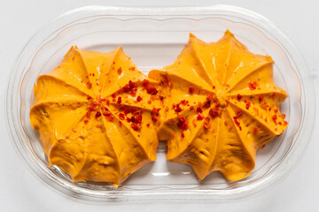 Orange antipasti cream topping with pepper pieces on top in a transparent plastic packaging view from top down.