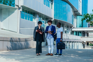 Obraz premium Businessman showing documents to his multi-ethnic co-workers in front of their big modern office building