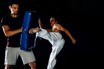 Male training session of a male fighter kicking a punching pad held by a couch