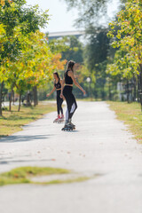 Rearview of two young fit women on roller skates riding outdoors on urban street in the park.