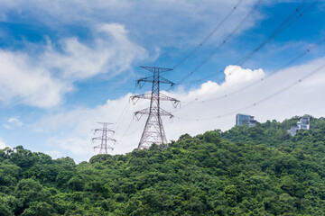 Electricity transmission tower and cable wire on the top of mountain with green forest against blue cloudy sky