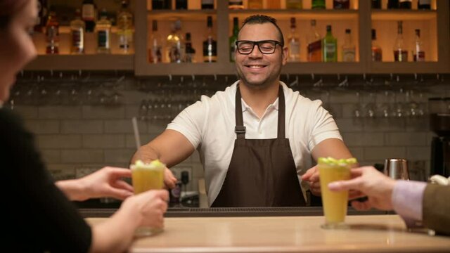 smiling black waiter serves cocktails to customers at the bar, close up