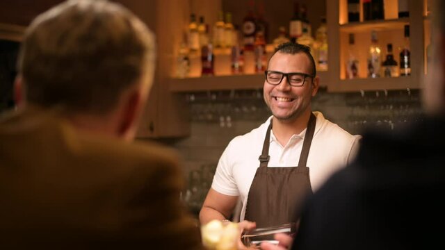 a smiling and sociable bartender conducts a conversation with customers in the bar. Evening in the restaurant, communication of bar guests with the bartender