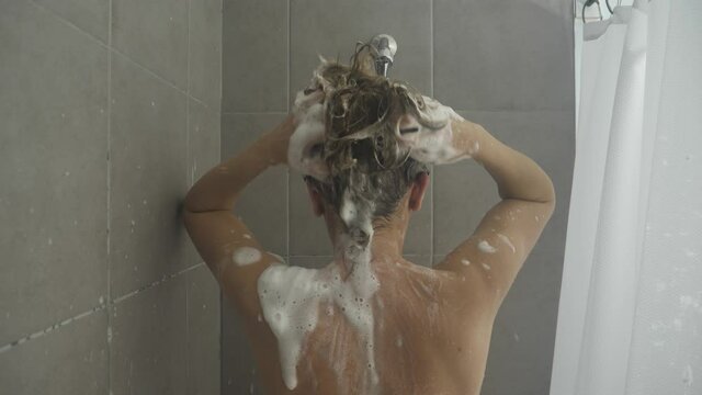 Middle age woman washing her beautiful hair with shampoo in the shower cabin