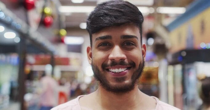 Young Brazilian man smiling in a marketplace. Latin man smiling to camera. 4K.