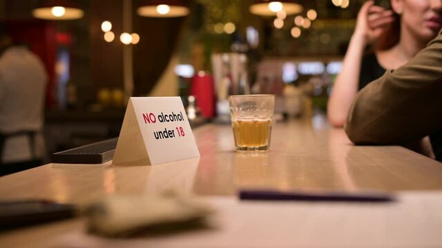 A sign with an age limit for the sale of alcohol is on the bar. The caption states that the bar does not sell alcohol to persons under the age of eighteen.