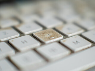 Very dirty white wireless computer keyboard with button J in focus