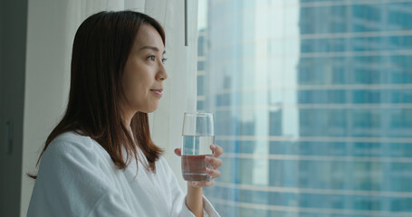 Woman look outside the window and hold a glass of water