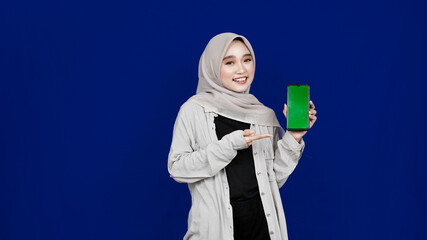asian hijab woman pointing hand phone with green screen isolated blue background