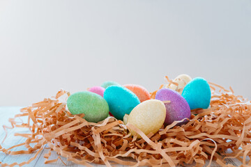Colorful Easter eggs in a nest, on a light wooden background.top view. Copy space.  
