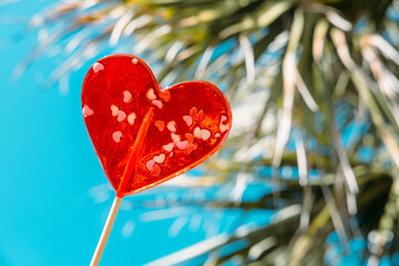 Banner of heart shaped lollipops on blue sky and palm background. Sun through colored hearts candies. Sweet Love. Valentine's Day. Valentines day card. 