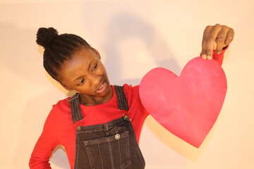 Confused girl holding up and looking at red heart sign indoors