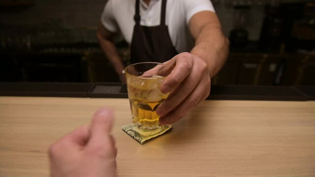 A drunken bar patron buys a drink with cash, first-person view. Man puts money on the bar and gets a drink from the bartender