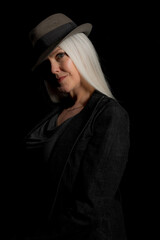 Image of a beautiful mature woman with platinum blonde hair, wearing a hat. Studio image with a black background.