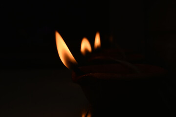 closeup of handmade lit three clay diya (lamp) in series with dark background for template and wallpaper