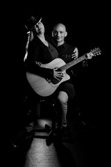 Fototapeta premium Image of a man and woman sitting in a dark room holding a guitar, creating art and music.