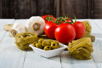 fresh tomato, garlic, olive, uncooked tagliatelle pasta on white wooden
