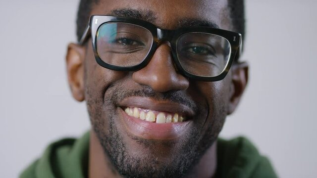 Portrait of handsome black man in glasses looking to camera before smiling, in slow motion