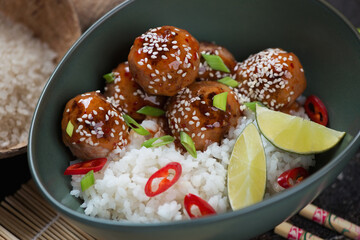 Close-up of a green bowl with asian-style white rice and meatballs in sweet and sour sauce, selective focus, studio shot