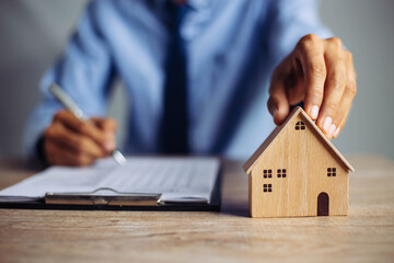 Businessman choosing mini wood house model from model on wood table, Planning to buy property....