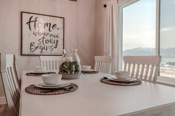 White table set for four persons inside dining room of home with large window