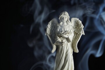 a photo of a figurine of a guardian angel surrounded by incense smoke on a black background