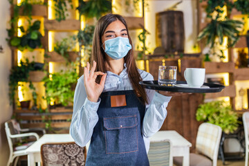 Female waitress in a medical protective mask serves the coffee in restaurant durin coronavirus...